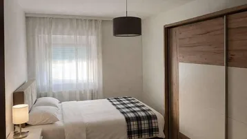 Helles Schlafzimmer mit Doppelbett, Holzschiebetürenschrank und Fenster mit Vorhängen.