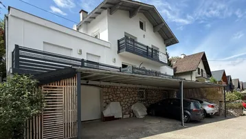 Weißes Wohnhaus mit Satteldach und integriertem Carport für mehrere Fahrzeuge auf dem Grundstück.