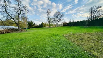 Große Rasenfläche mit Bäumen und Hecken, umgeben von einer ländlichen Landschaft unter blauem Himmel.
