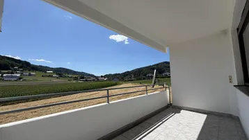 Geräumiger Balkon mit Fliesenboden und weitem Blick über Felder und grüne Hügel.