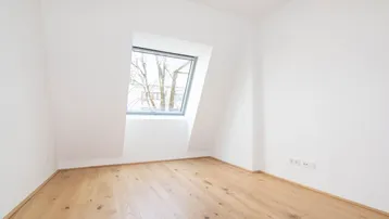 Helles Zimmer im Dachgeschoss mit Holzboden und schrägem Fenster, ideal als Schlafzimmer oder Büro.