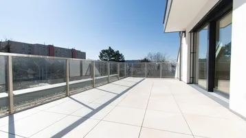 Geräumige Sonnenterrasse mit modernen Fliesen und Glasgeländer, ideal für Entspannung im Freien.