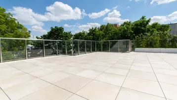 Geräumige Dachterrasse mit modernen Fliesen und Glasgeländer unter blauem Himmel.