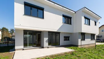 Moderne Architektur eines Neubaus mit weißer Fassade, großen Fenstern und einer Terrasse.