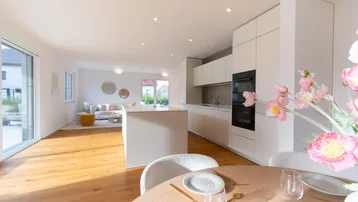 Moderne offene Wohnküche mit Essbereich, Holzboden und Zugang zur Terrasse.