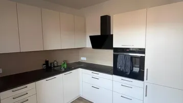 Moderne Küche mit weißen Schränken, dunkler Arbeitsplatte, integrierten Geräten und Laminatboden.