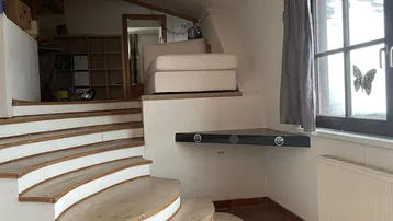 Gemütlicher Wohnbereich mit einzigartiger Holztreppe, Dachschrägen und Blick nach draußen.