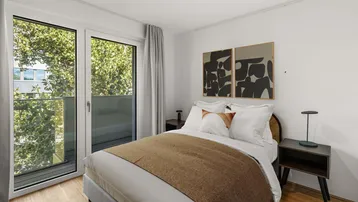 Helles Schlafzimmer mit Holzboden, modernem Bett und Zugang zum Balkon.