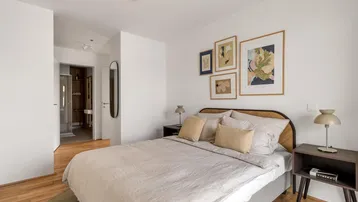 Helles Schlafzimmer mit Holzboden, modernen Kunstwerken und Zugang zu einem angrenzenden Bad.