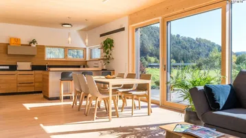 Heller offener Wohn- und Essbereich mit Holzböden, moderner Küche und großem Schiebefenster mit Blick ins Grüne.