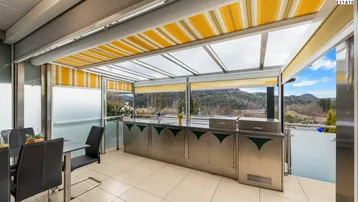 Geräumige verglaste Terrasse mit Essbereich, Außenküche und Panoramablick auf die Landschaft.