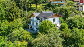 Modernes Wohnhaus mit mehreren Balkonen und Photovoltaikanlage, umgeben von üppiger Vegetation.