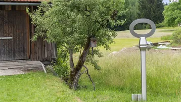 Große Metallschlüssel-Skulptur in einer grünen Wiese neben einem Baum mit Vogelhaus, vor dem Haus.