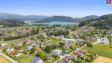 Weitläufige Luftaufnahme der Wohnsiedlung mit See- und Bergblick in sonniger Landschaft.