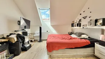 Helles Schlafzimmer im Dachgeschoss mit Dachfenster, Holzboden und schrägen Wänden.
