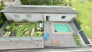 Gartenbereich mit Swimmingpool und gepflasterter Terrasse, umgeben von viel Grün.