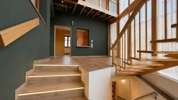 Geräumiger Eingangsbereich mit moderner Holztreppe, integrierter Beleuchtung und hohen Decken.