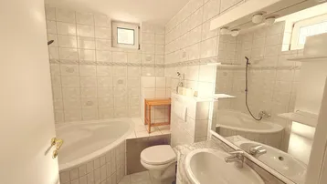 Helles Badezimmer mit Eckbadewanne, WC, Waschbecken, Spiegel und gefliesten Wänden.