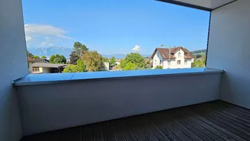 Heller Balkon mit Holzboden und weitem Blick auf die umliegende Landschaft und Berge.