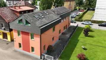 Luftaufnahme eines Wohnhauses mit auffälliger orangefarbener Fassade und grünen Fensterrahmen.
