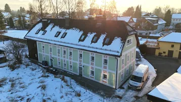 Historisches Gebäude mit hellgrüner Fassade, verschneitem Dach und ländlicher Umgebung.