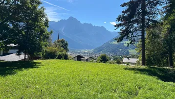 Grünes Grundstück mit weitem Blick auf die umliegende Berglandschaft und ein Dorf im Tal.