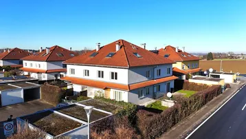 Luftaufnahme einer Wohnsiedlung mit Reihenhäusern, roten Dächern und Garagen in ländlicher Umgebung.