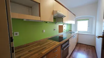 Funktionale Küche mit Holz-Arbeitsplatte, grüner Rückwand und Fenster für Tageslicht.