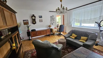 Helles Wohnzimmer mit Parkettboden, Ledersofa, Schreibtisch und einem großen Fenster.