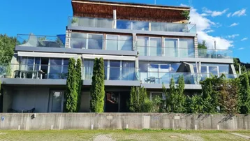 Moderne Terrassenwohnungen mit Glasbalkonen und großen Fensterfronten unter blauem Himmel.