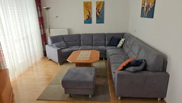 Gemütliches Wohnzimmer mit großem Ecksofa, Holzboden und viel Tageslicht durch das Fenster.