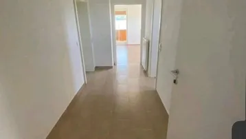 Heller Flur mit beigefarbenen Fliesen, weißen Wänden und Zugang zu verschiedenen Räumen.