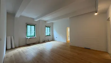 Heller, leerer Raum mit Holzbalkendecke und neu verlegtem Parkettboden, bereit für den Ausbau.
