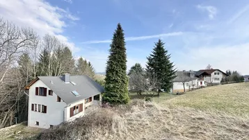 Weitläufiger Blick über die grüne Landschaft mit einem benachbarten Haus und hohen Bäumen.