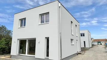 Modernes, neu gebautes Einfamilienhaus mit heller Fassade und großen Fenstern in einer Neubausiedlung.