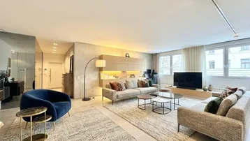 Geräumiges Wohnzimmer mit modernen Möbeln, hellen Teppichen und großen Fenstern für viel Tageslicht.
