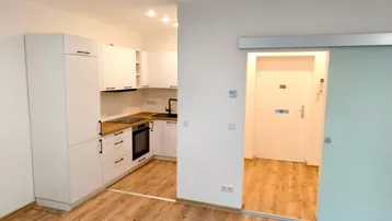 Moderne Einbauküche in Weiß mit Holz-Arbeitsplatte und Zugang zum Flur durch eine Glasschiebetür.
