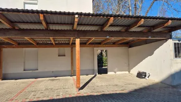 Überdachter Stellplatz mit Holzkonstruktion und gepflastertem Boden vor einem Wohngebäude.