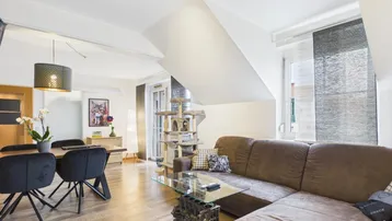 Heller Wohn- und Essbereich mit Holzboden, gemütlichem Sofa und Esstisch unter Dachschrägen.