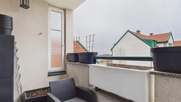 Kleiner Balkon mit Sitzgelegenheit und Pflanzenkübeln, Blick auf umliegende Dächer.