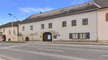 Historisches Gebäude mit Putzfassade, Holztoren und Fensterläden an einer Hauptstraße gelegen.