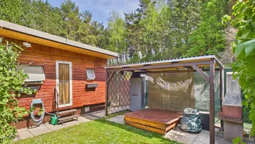 Kleiner Gartenbereich mit Rasenfläche, überdachtem Sitzplatz und einem Grill neben einer Holzhütte.