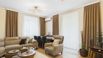 Helles Wohn- und Esszimmer mit beigem Sofa, Holzboden und modernen Deckenleuchten.