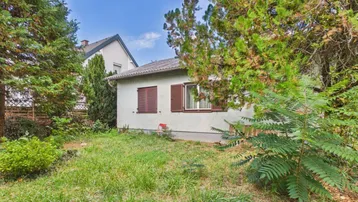 Kleines Einfamilienhaus mit grünem Garten und Bäumen in ländlicher Umgebung.
