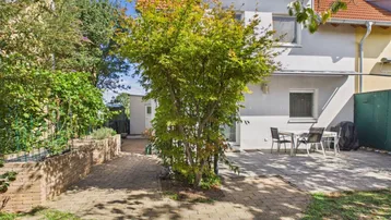 Hinterhof mit gepflasterter Terrasse, Gartenmöbeln und einem Baum, ideal für Entspannung im Freien.