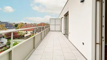 Geräumiger Balkon mit Fliesenboden und Blick auf die umliegende Wohngegend unter blauem Himmel.