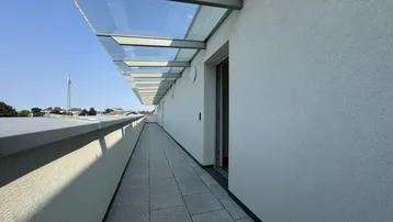 Langer, schmaler Balkon mit Glasüberdachung und Blick auf die Umgebung.