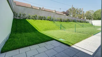 Gepflegte Rasenfläche mit gepflastertem Weg und einer Mauer im Hintergrund, ideal für Entspannung.