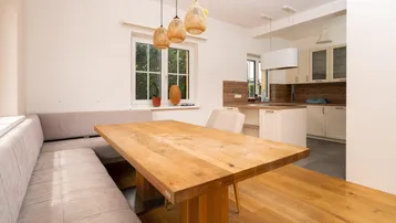 Heller Essbereich mit Holztisch und Sitzbank, offen zur modernen Küche mit Holzakzenten.