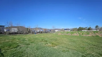 Weitläufige grüne Wiese mit Blick auf die umliegende Landschaft und ferne Berge unter blauem Himmel.